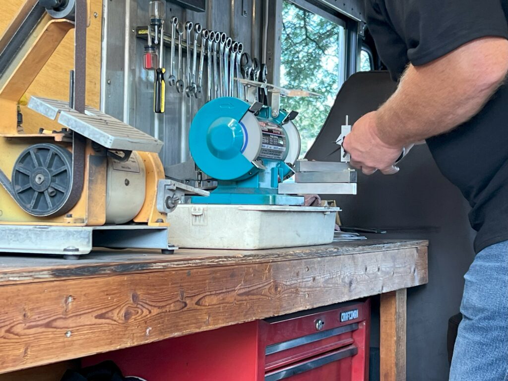 Man sharpening tool on bench grinder in workshop.