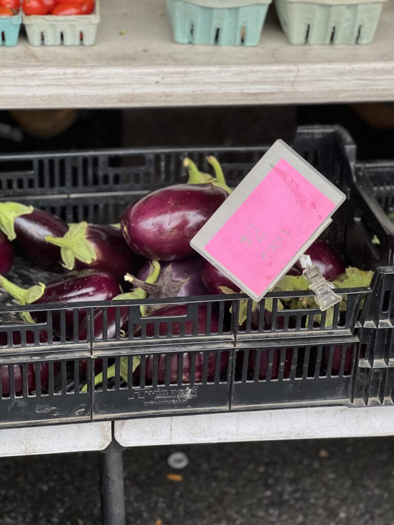 Fresh eggplants for sale at market, $2 each sign.