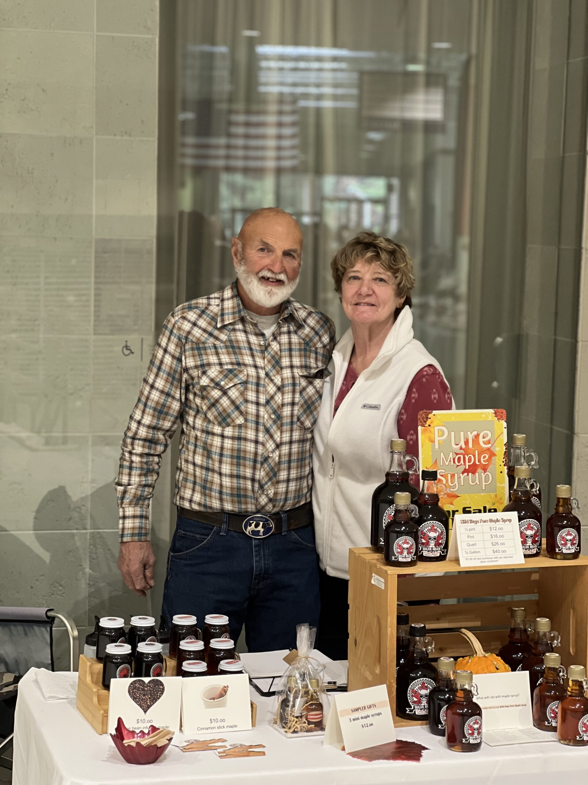 Couple selling maple syrup at local market booth.