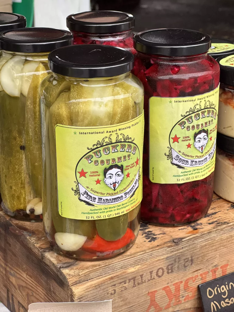 Jars of pickled cucumbers and vegetables on wooden shelf.