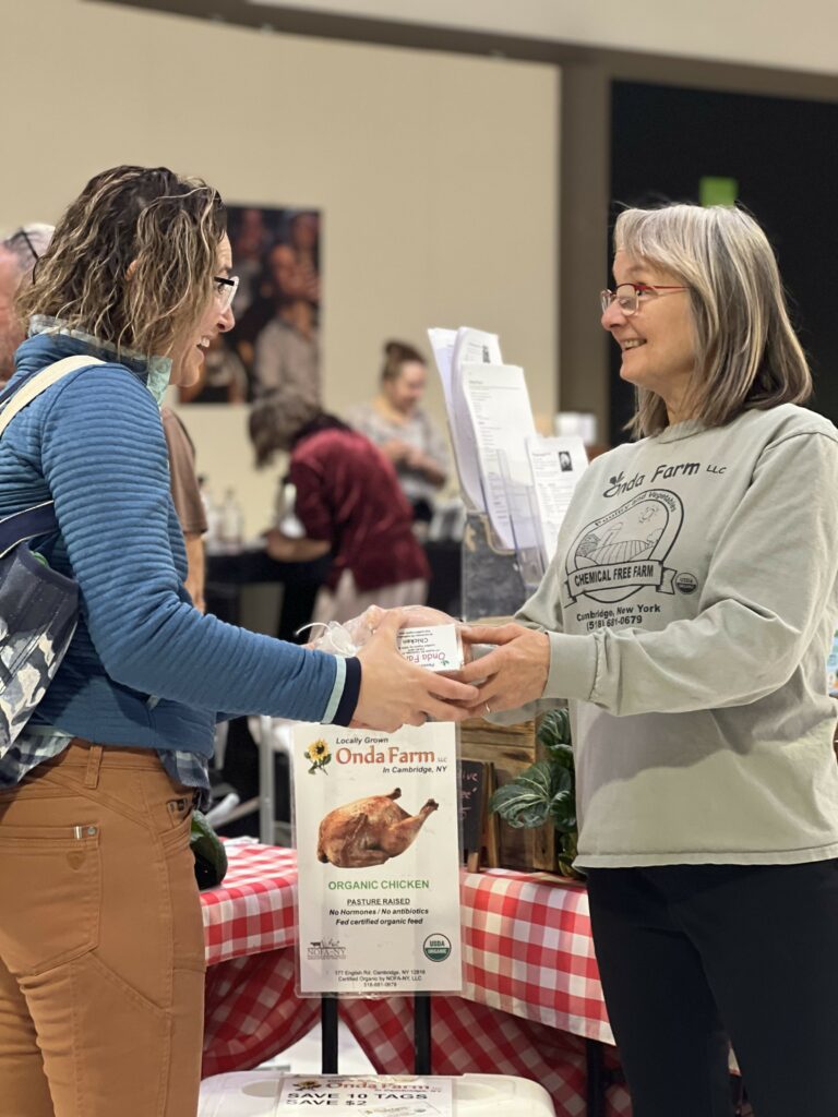 Two women discussing organic chicken at a farm booth.