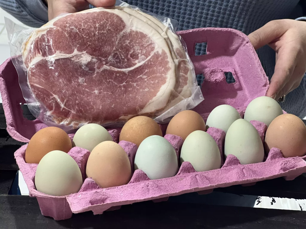 Eggs in carton and ham slice held by person.